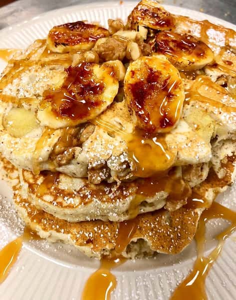 a stack of pancakes with bananas and maple syrup