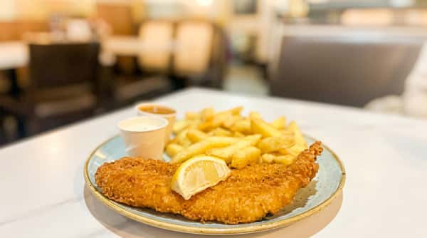 Fish and chips with a lemon wedge and tartar sauce on a light blue plate.