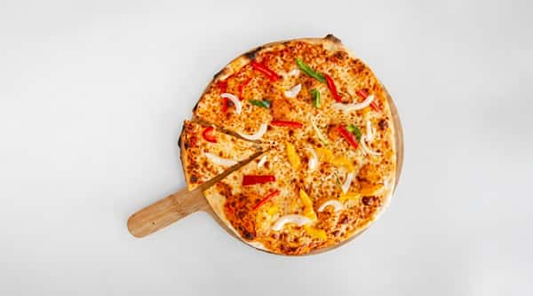 Whole pizza with melted cheese, red, green, and yellow bell peppers, and onions on a wooden pizza peel.