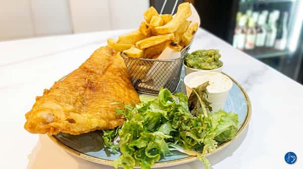 Fish and chips with mushy peas, tartar sauce, and a side salad on a round plate.