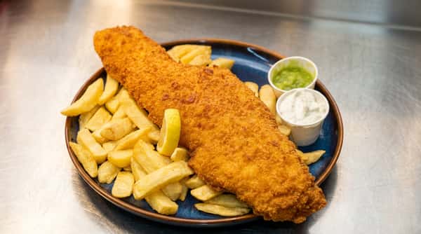 Fish and chips on a blue plate with a lemon wedge, mushy peas, and tartar sauce.