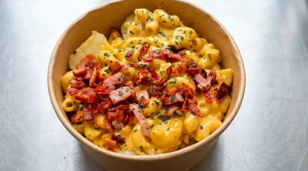 Mac and cheese with bright yellow cheese sauce, topped with crumbled bacon and green herbs in a bowl.