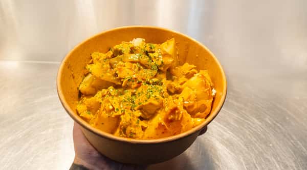 Chicken curry with potato chunks, garnished with parsley, served in an orange paper bowl.