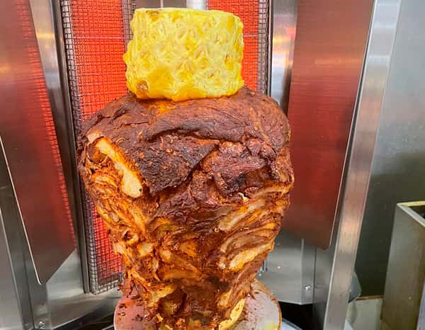 Juicy al pastor pork stacked on a vertical spit, marinated in smoky adobo spices and topped with fresh pineapple, ready for authentic tacos at Tacos Chano.