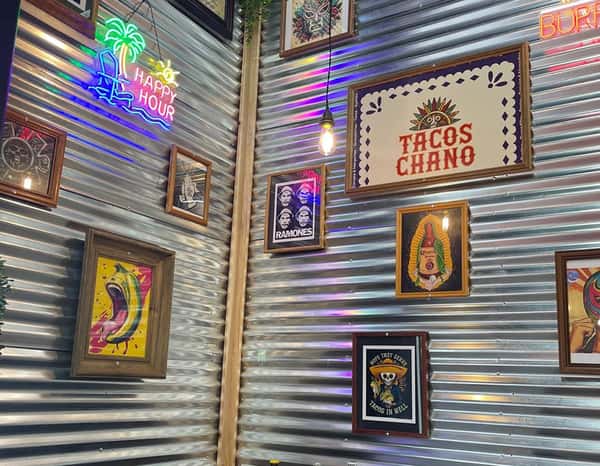Colorful interior of Tacos Chano with neon signs, vibrant Mexican-themed artwork, and corrugated metal walls, creating a lively and festive dining atmosphere.
