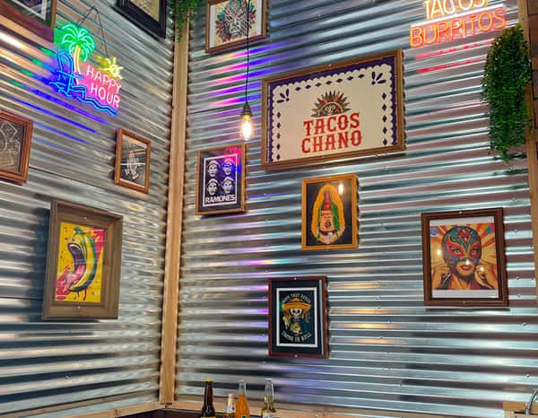 Colorful interior of Tacos Chano with neon signs, vibrant Mexican-themed artwork, and corrugated metal walls, creating a lively and festive dining atmosphere.