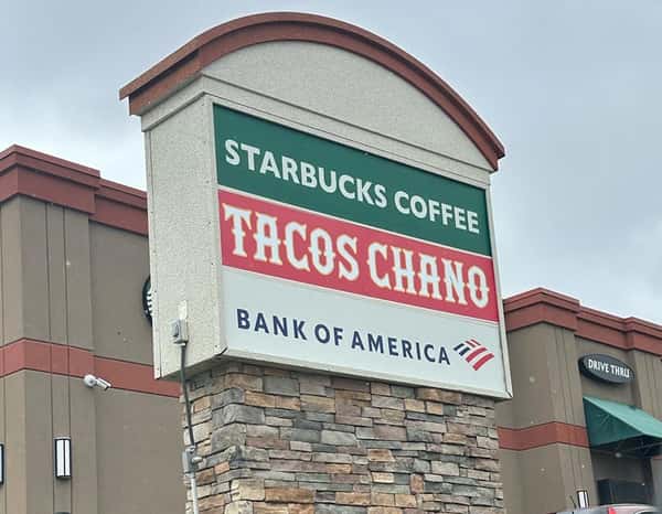 Outdoor shopping center sign featuring Starbucks Coffee, Tacos Chano, and Bank of America, with a stone base and drive-thru visible in the background.