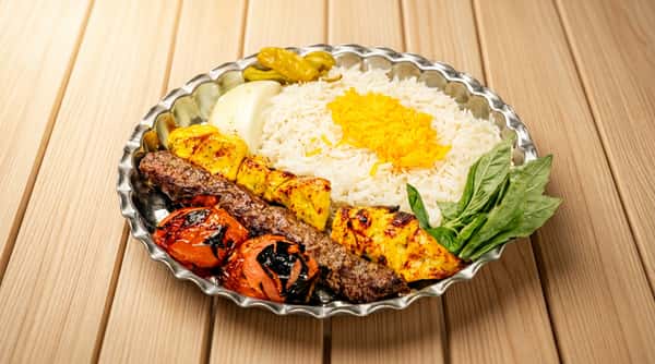 Persian kebab platter with basmati rice, saffron, grilled tomatoes, ground meat skewer, chicken pieces, onion, and herbs.