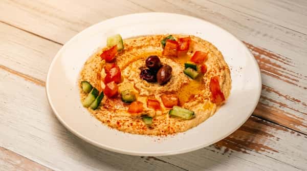Hummus drizzled with olive oil, garnished with diced tomatoes, cucumbers, olives, and paprika.