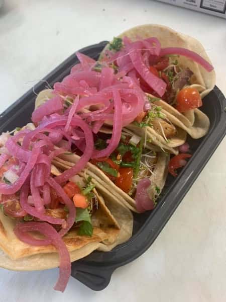 4 tacos in corn tortillas topped with pickled red onion, cilantro and tomato