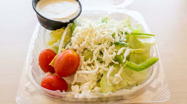 Side salad with lettuce, green peppers, cherry tomatoes, shredded white cheese, and a cup of ranch dressing.
