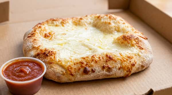 Khachapuri with melted cheese, a pizza cutter, and a side of red sauce in a cup.