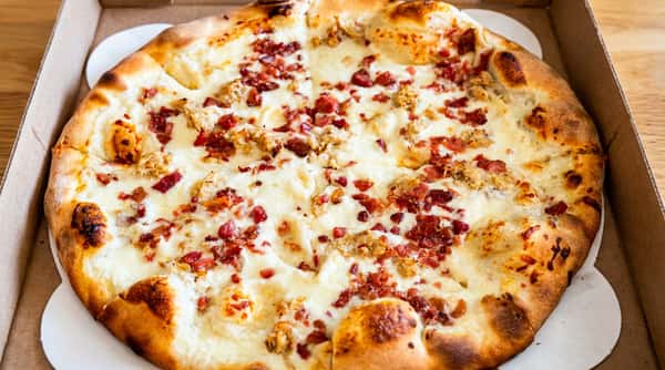 Pizza with mozzarella, crumbled bacon, and chicken on a white crust, sliced in a box.