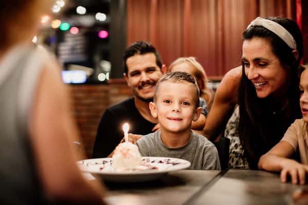 Family gathered around a restaurant table with a birthday cake and balloons, celebrating together in Oviedo, FL