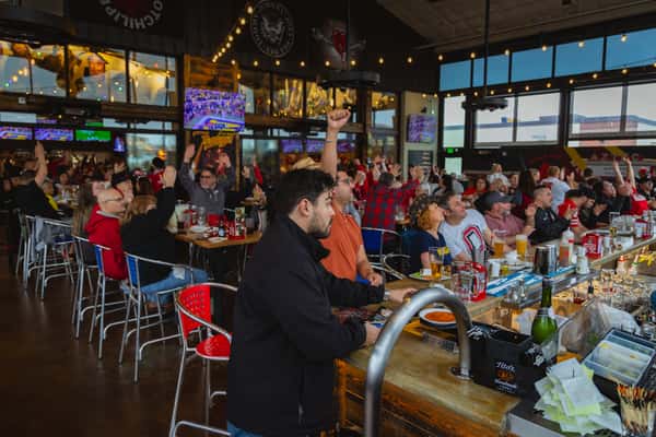 Crowd of guests filling the patio room and watching a game on the wall of TVs above the bar in Grapevine, TX