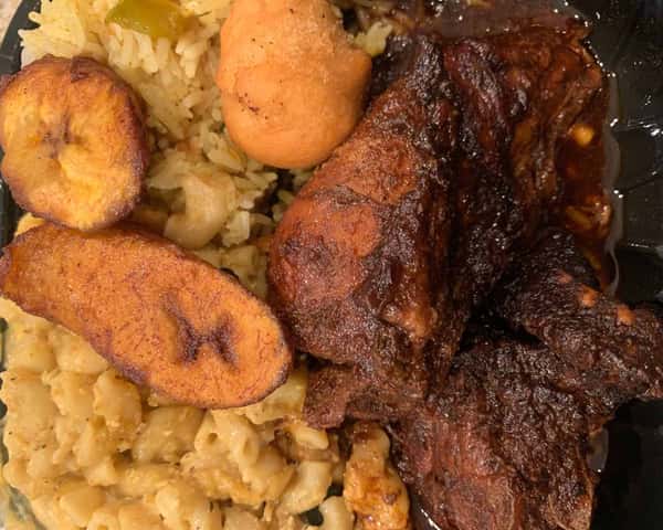 Jamaican meal with jerk chicken, fried plantains, rice, mac and cheese, and a festival dumpling on a black plate.