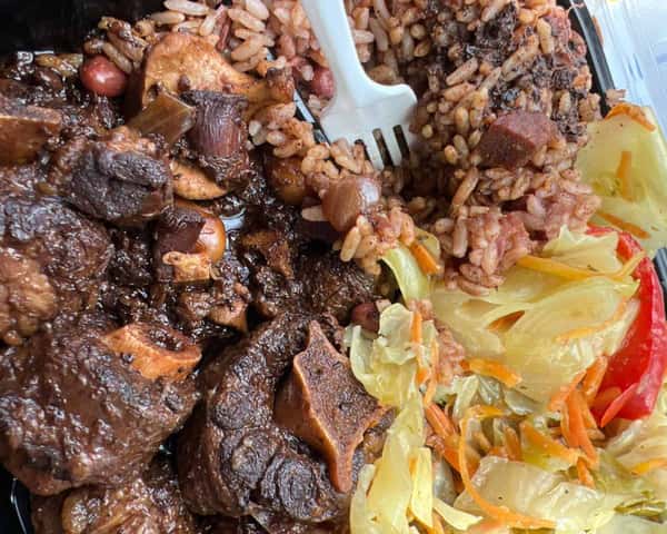 This hearty Jamaican meal features tender oxtail stewed in rich gravy, served with rice and peas and a side of steamed cabbage and carrots.