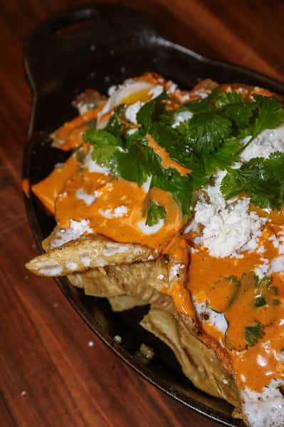 Chilaquiles topped with fried eggs, queso fresco, fresh cilantro, and drizzled with a creamy red sauce and green salsa.