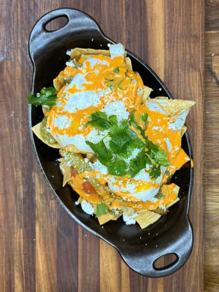 Chilaquiles topped with fried eggs, queso fresco, fresh cilantro, and drizzled with a creamy red sauce and green salsa.