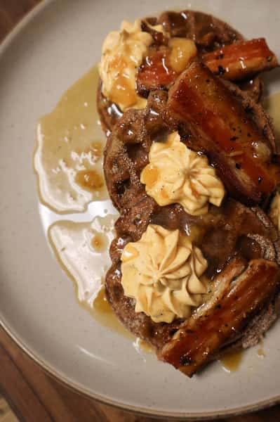 Stack of waffles topped with caramelized bananas, whipped cream, and syrup on a ceramic plate.