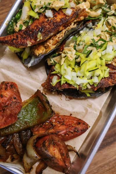 Blackened fish tacos with shredded cabbage and diced onions, served with roasted peppers, tomatoes, and onions.