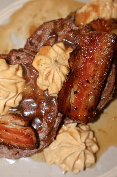 Stack of waffles topped with caramelized bananas, whipped cream, and syrup on a ceramic plate.