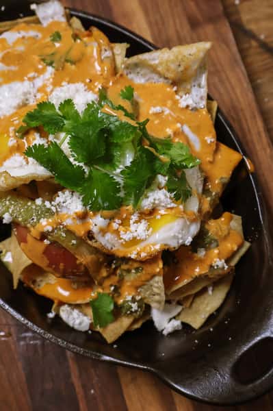 Chilaquiles topped with fried eggs, queso fresco, fresh cilantro, and drizzled with a creamy red sauce and green salsa.