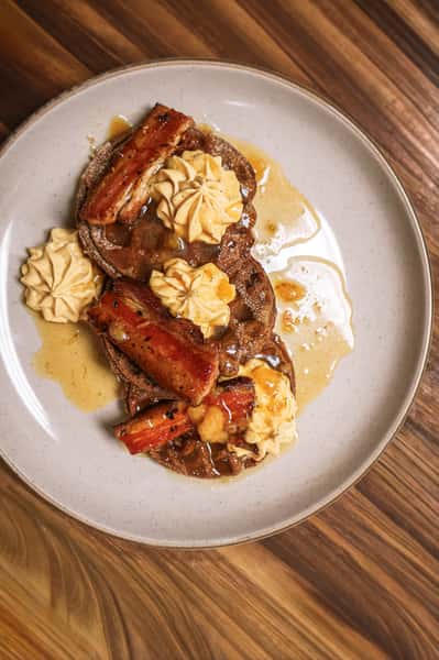 Stack of waffles topped with caramelized bananas, whipped cream, and syrup on a ceramic plate.