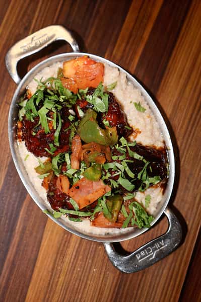 Braised beef short ribs served over creamy grits with sautéed peppers, tomatoes, and fresh cilantro garnish.