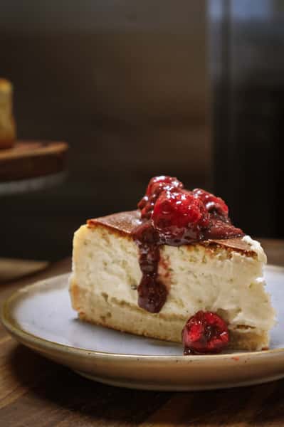 Slice of cheesecake topped with raspberry compote on a ceramic plate.