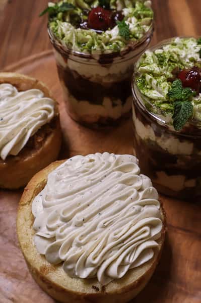 Mini cakes with piped vanilla frosting and layered dessert jars topped with whipped cream, mint, and cherries.