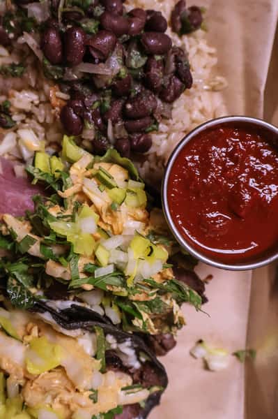 Chicken tacos with cilantro and onions, served with rice, black beans, and a side of red salsa.