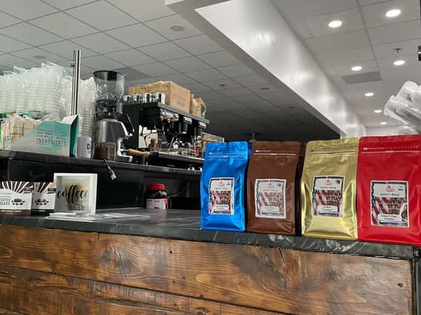 Liberty Brew coffee display on a wooden counter featuring four vibrant bags—blue, brown, gold, and red—showcasing their patriotic-themed blends in a cozy café setting.