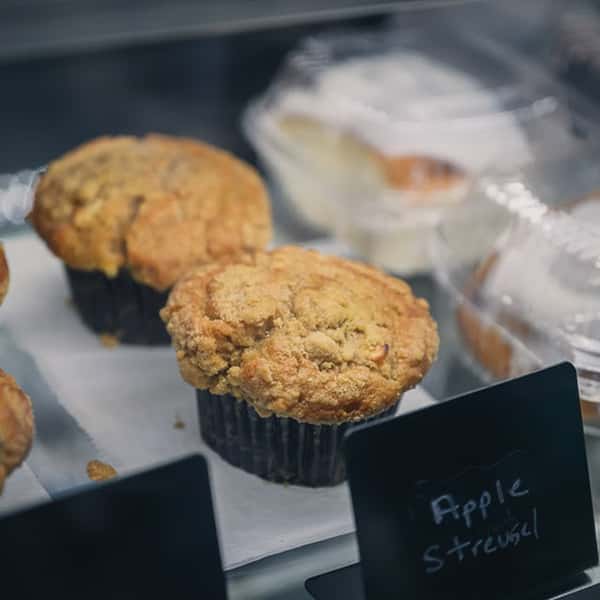 Freshly baked apple streusel muffins with a crumb topping on display in a glass bakery case at Liberty Brew café.