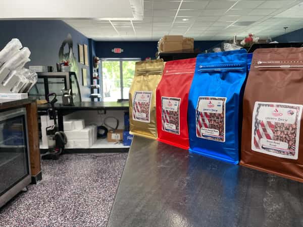 Colorful display of Liberty Brew's signature coffee blends—gold, red, blue, and brown bags—lined up on a counter in a veteran-owned coffee shop.