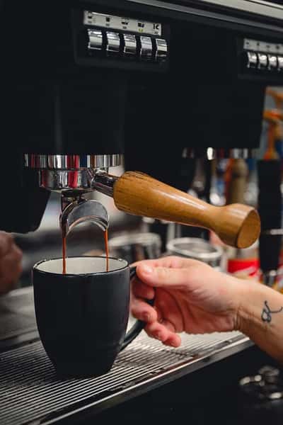 Close-up of espresso being freshly pulled into a black ceramic mug from a professional espresso machine at Liberty Brew coffee shop.