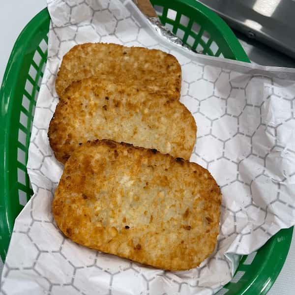 Three golden-brown crispy hash browns served in a green basket lined with white parchment paper—perfect as a savory breakfast side.