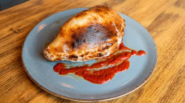 Calzone with browned crust and crimped edges, served on a blue plate with a streak of red marinara sauce.