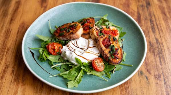 Burrata salad with arugula, toasted bread, cherry tomatoes, and balsamic drizzle on a teal plate.