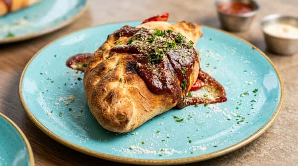 Baked calzone with a dark sauce, grated cheese, and green herbs on a teal plate.
