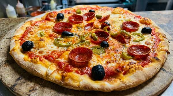Pepperoni pizza topped with melted cheese, black olives, and green peppers on a white surface.