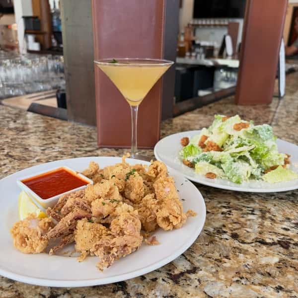 A plate of calamari and salad on a tabletop with a martini