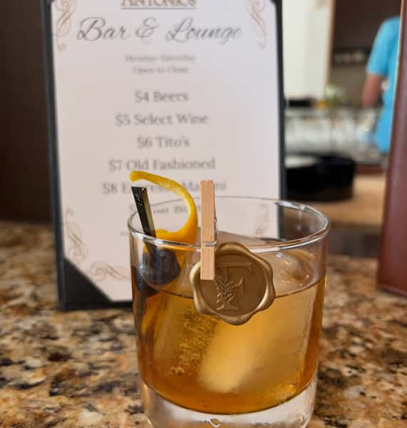 A specialty cocktail on a bar countertop with a menu in the background from Antonio's