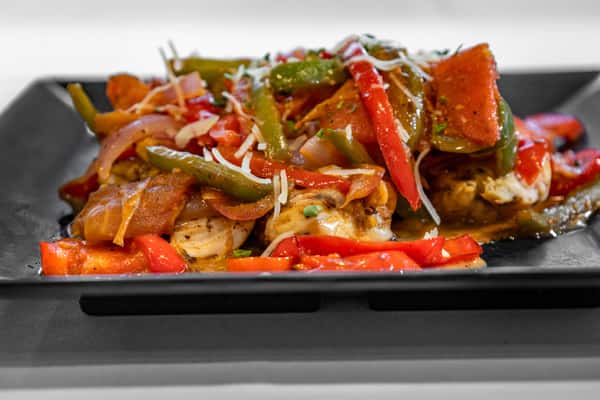 Grilled chicken breast topped with sautéed bell peppers, onions, and shaved parmesan, served on a black square plate for a colorful, zesty entrée.