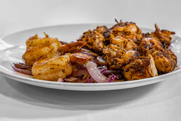 Seasoned grilled shrimp and Cajun chicken served with sautéed red onions on a white plate for a bold, Southern-inspired entrée.