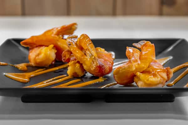 Golden fried shrimp drizzled with tangy bang bang sauce, artfully plated on a black square dish for a bold, flavorful starter.
