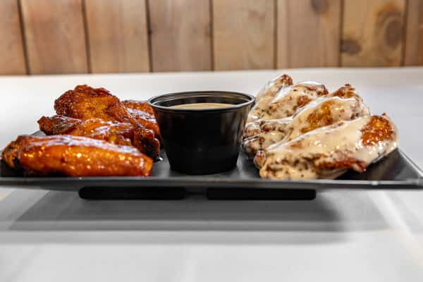 Appetizer plate with a variety of sauced chicken wings including buffalo and creamy ranch, served with dipping sauce on a black platter.