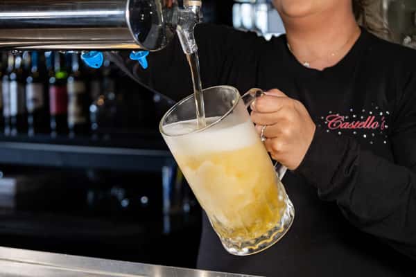 Castello's bartender pouring a frosty glass of draft beer from the tap, with overflowing foam and chilled mug in hand.