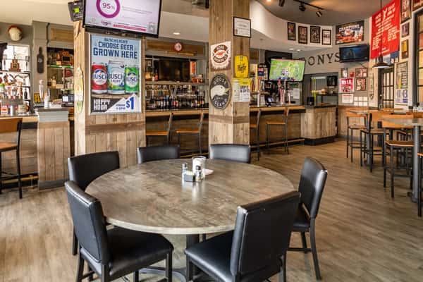 Casual sports bar dining area with wooden accents, round and high-top tables, and flat-screen TVs displaying live games above the bar.