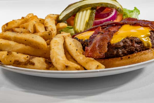 Juicy bacon cheeseburger with cheddar, pickles, lettuce, tomato, and onion, served with crispy seasoned fries on a white plate